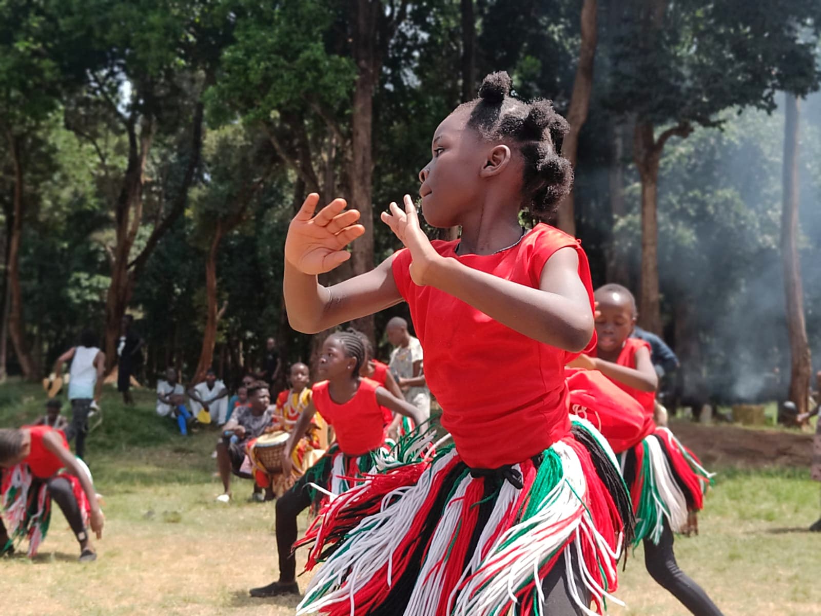 A young Nafsi dancer mid-step in raffia costume, drummers behind her