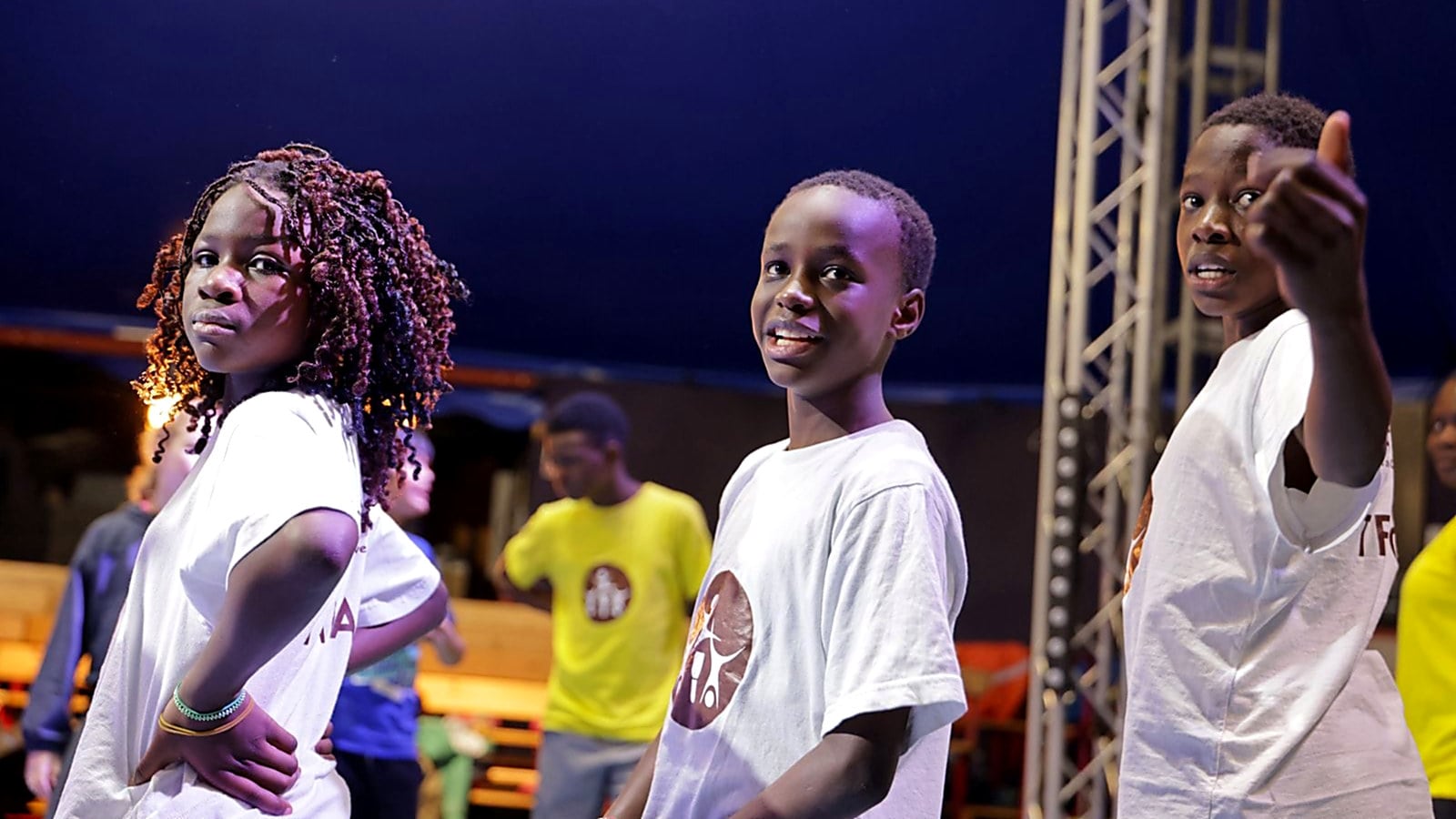 Three young Nafsi performers in Nafsi T-shirts on stage under the big top